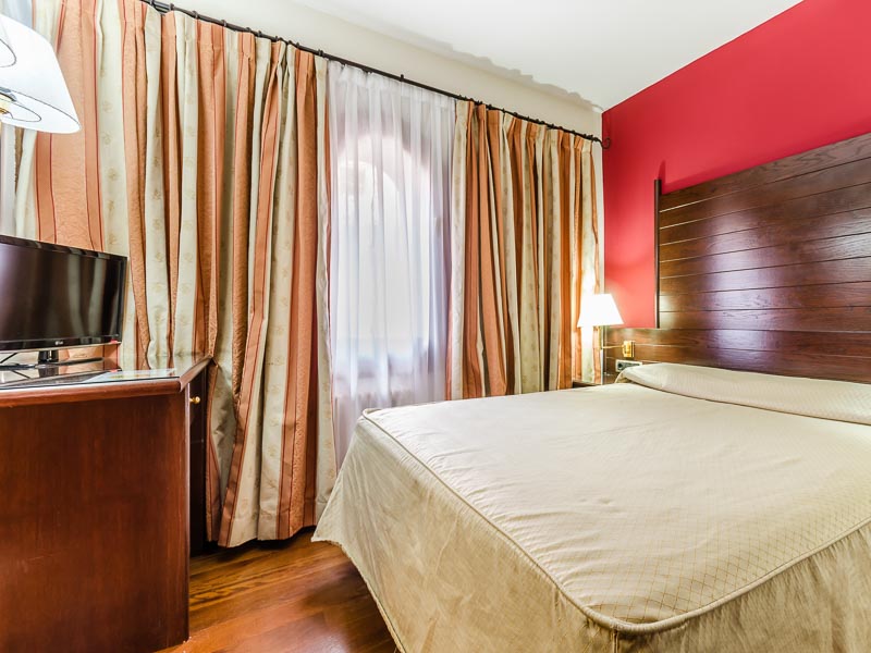 Habitación doble del Hotel Albarracín con pared roja y mobiliario de madera