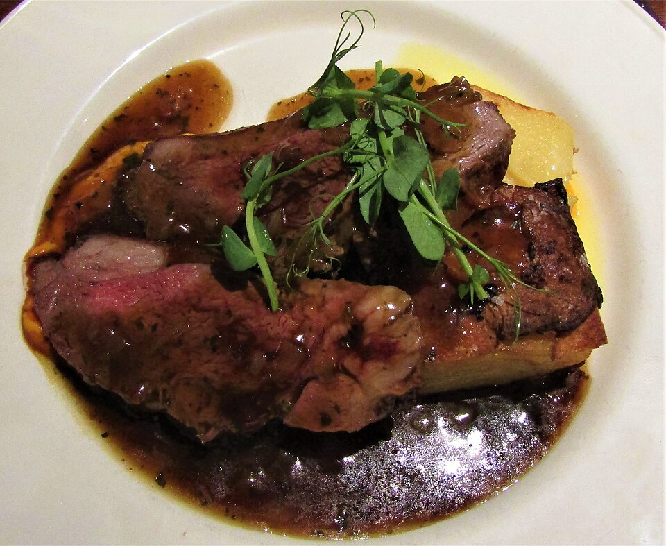 Plato de cordero asado servido con salsa, patata y brotes verdes