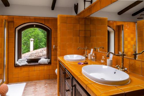 Baño con azulejos naranjas, dos lavabos y ventana en Can Serola, en Sales de Llierca
